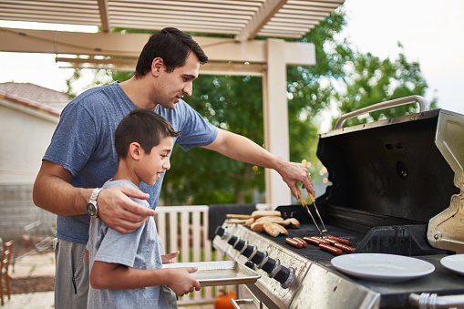 father teaching son how to grill hot dogs and bonding during the day